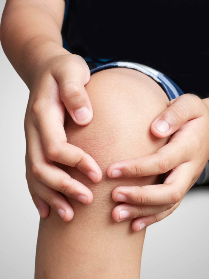 child holding sore knee with knee pain