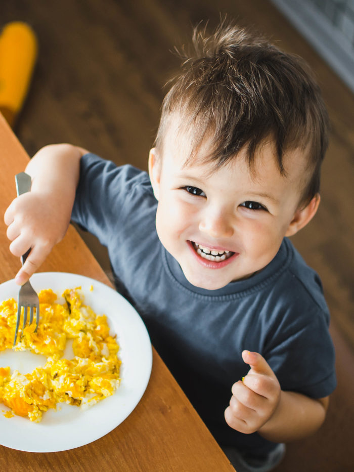 a child in a t-shirt in the kitchen eating an omelet