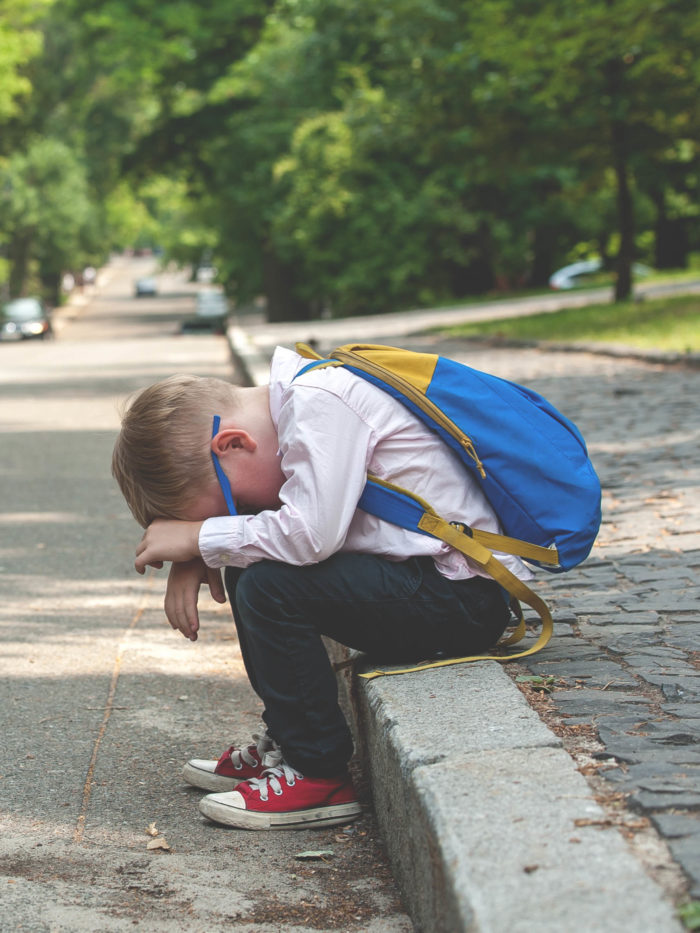 little boy crying on the curb while waiting for the school bus