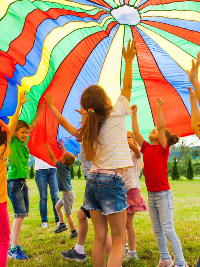 Joyous classmates jumping under colorful parachute