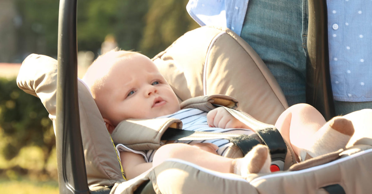 Mother holding child safety seat with baby near car outdoors