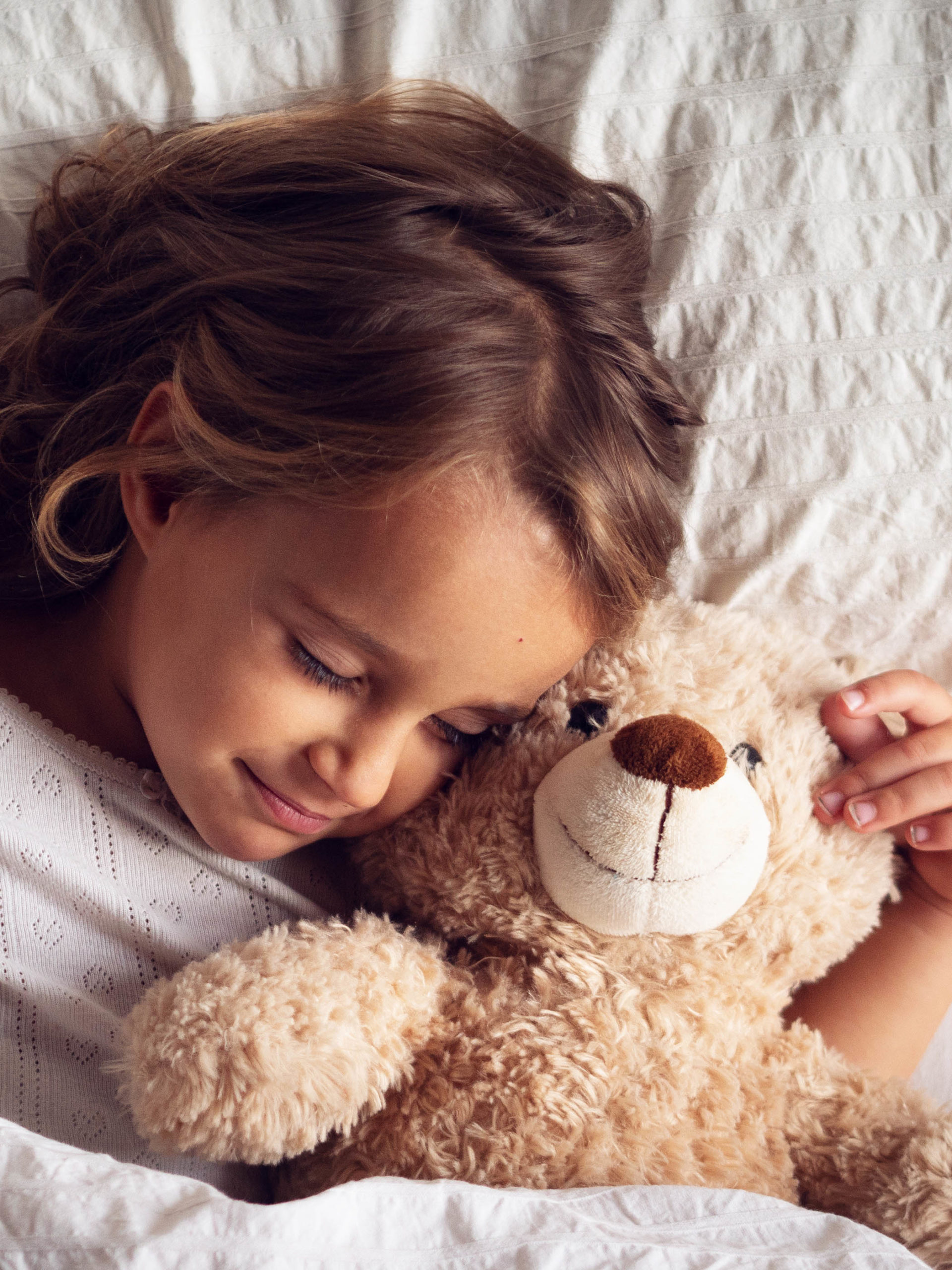 A girl sleeps in bed hugging her teddy bear
