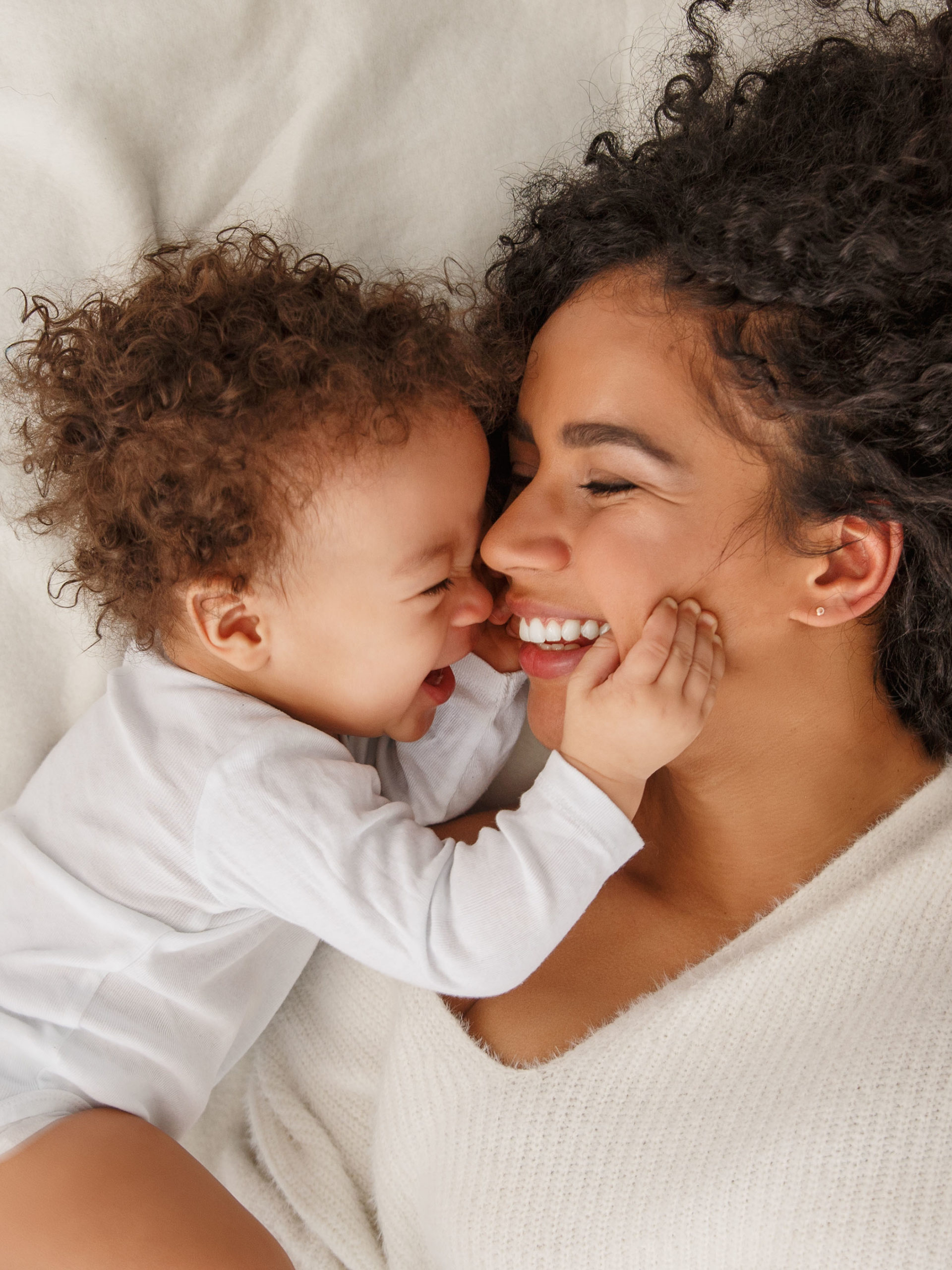 mother and baby smiling and cuddling face to face in bed
