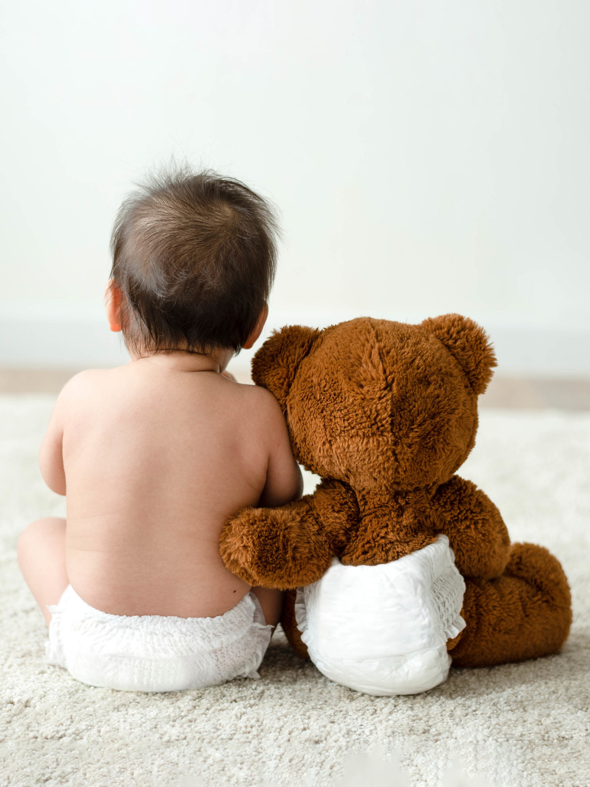 Toddler sitting beside his teddy bear who has his furry hand on his back