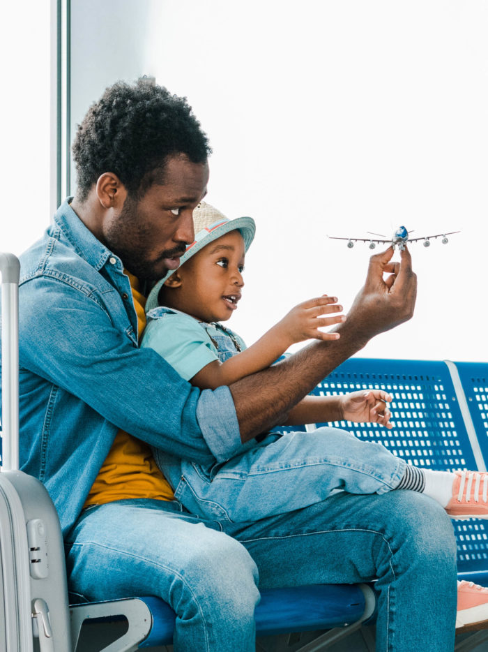 father and son sitting with suitcase in airport and playing with toy plane