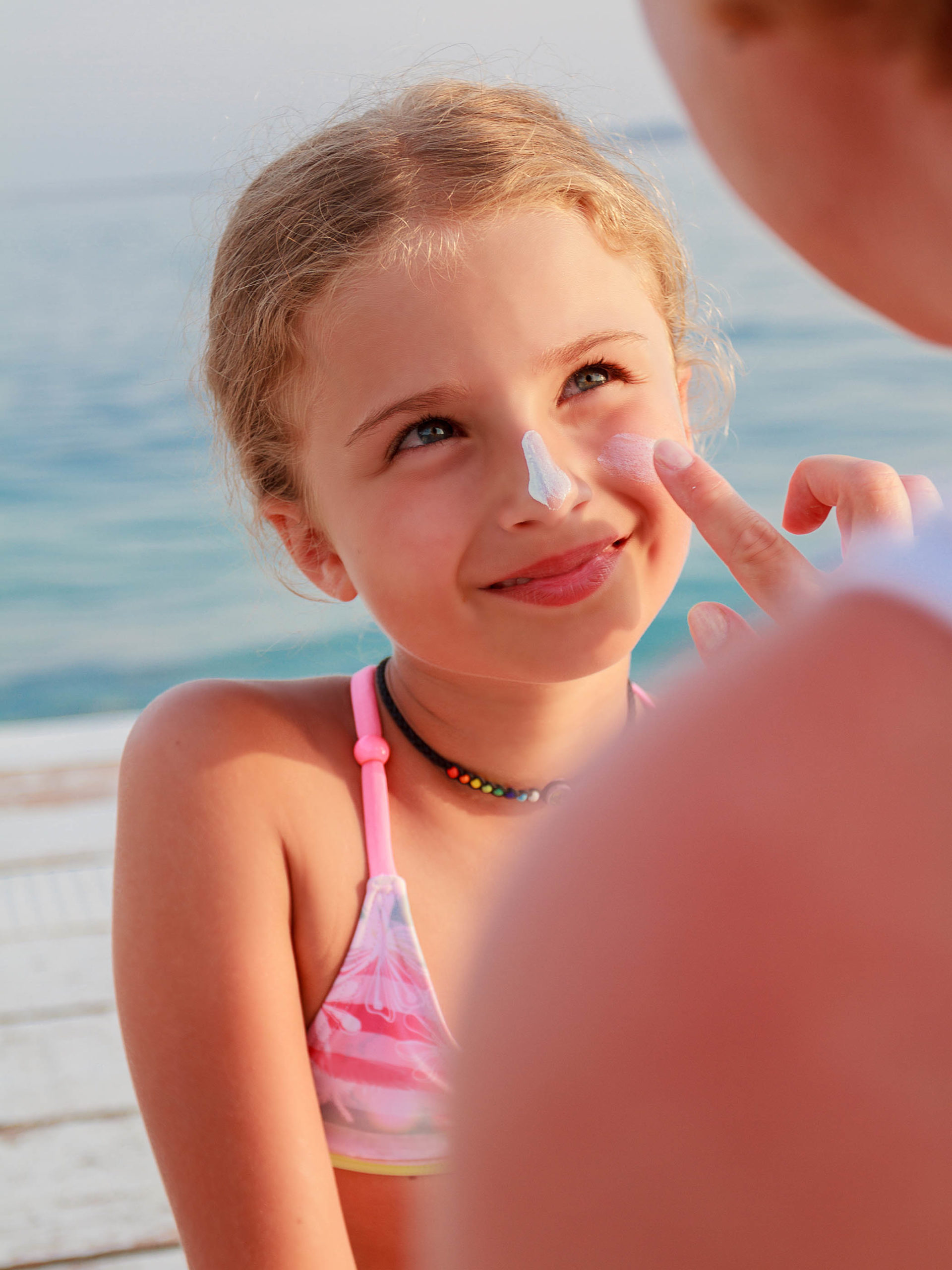 mother applies sunscreen to daughters face at the beach