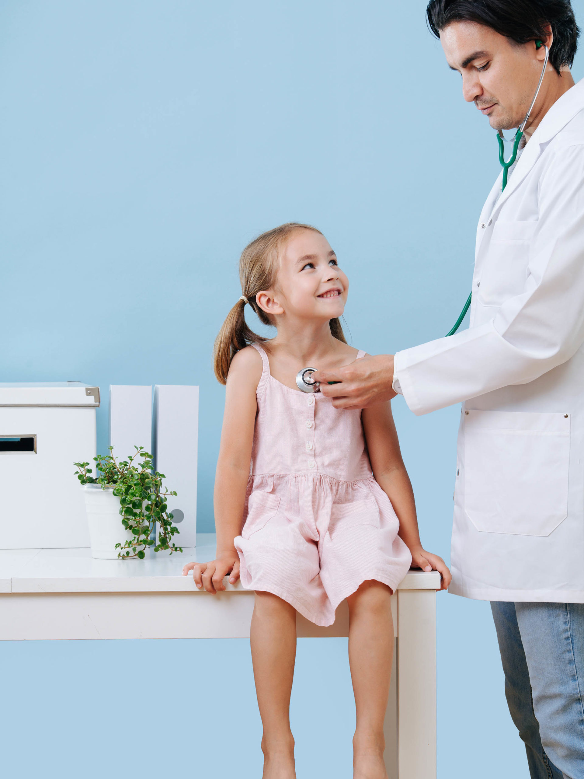 doctor examining a cheerful first grader child girl with a stethoscope