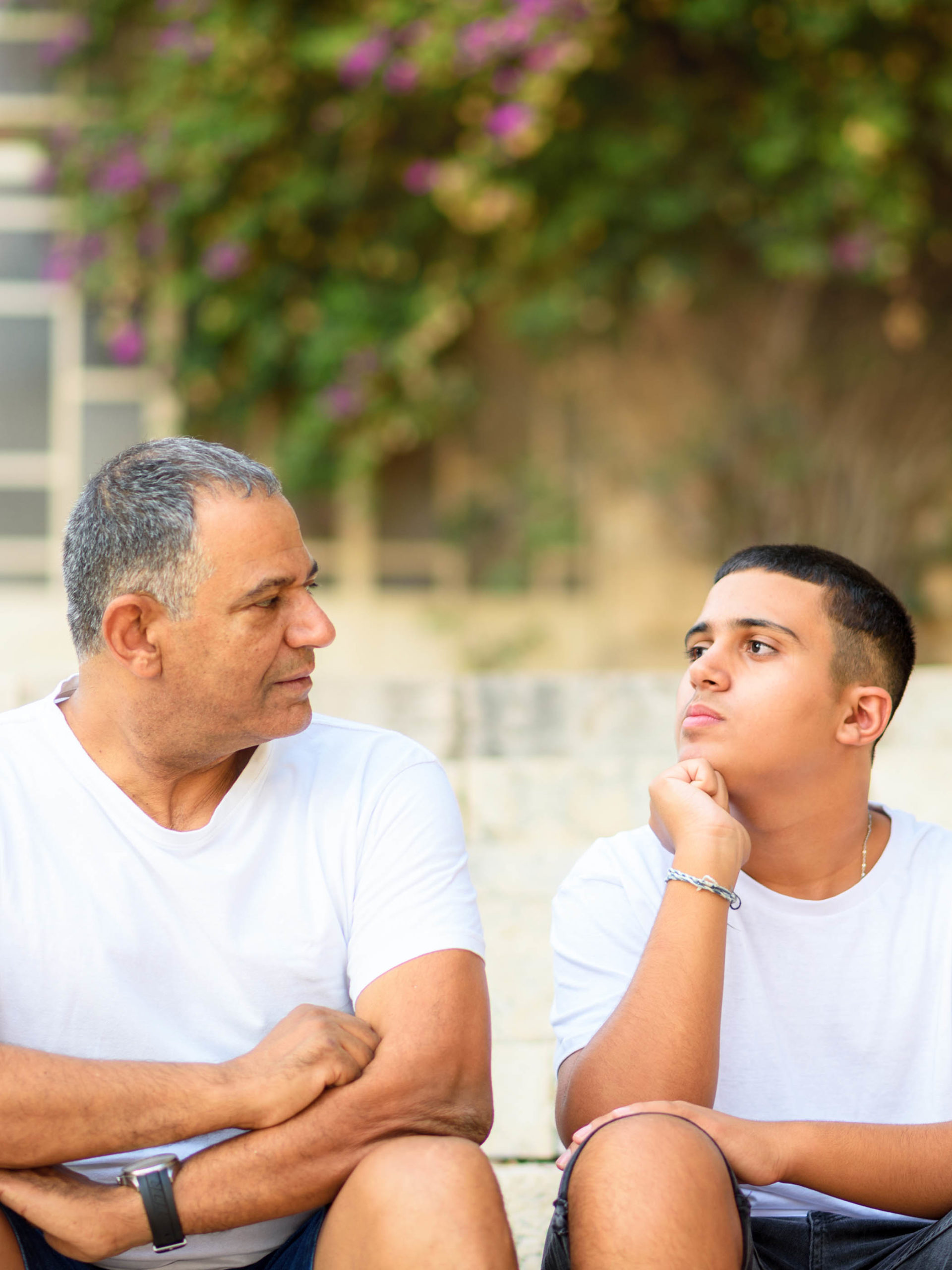 Teenage son and father sitting on stairs outdoors talking