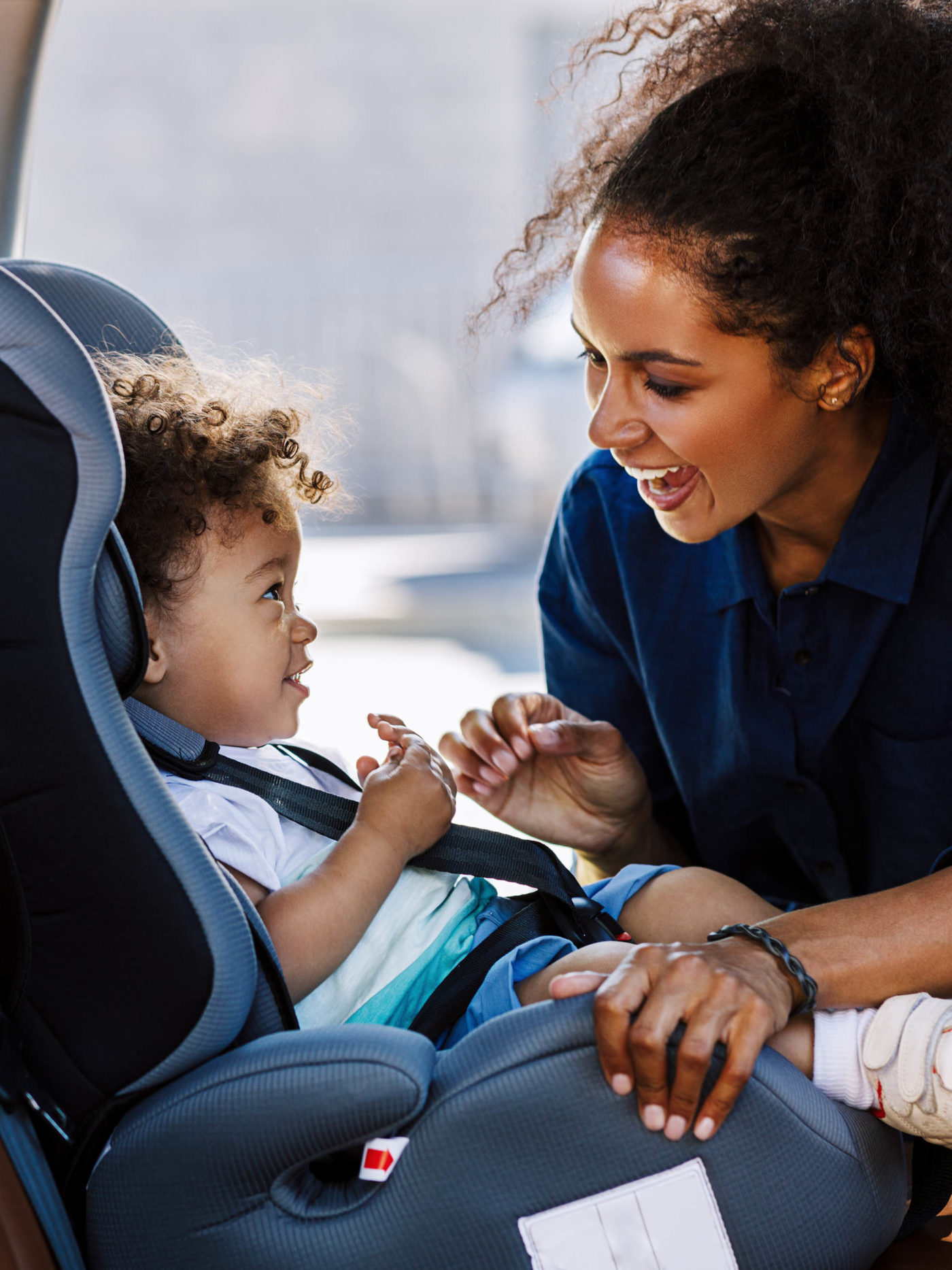 Young female preparing kid for a trip putting him into a car seat