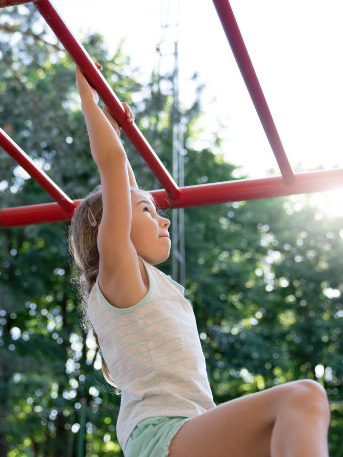 little girl hanging on monkey bars at the playground