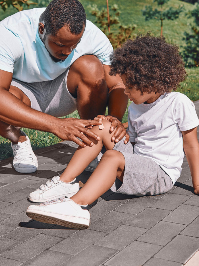 father squatting next to his kid while checking his knee for injuries