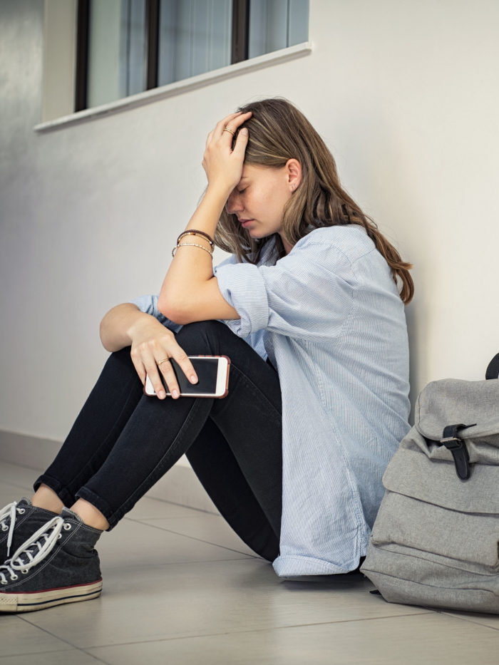 Upset and depressed girl holding smartphone sitting on floor