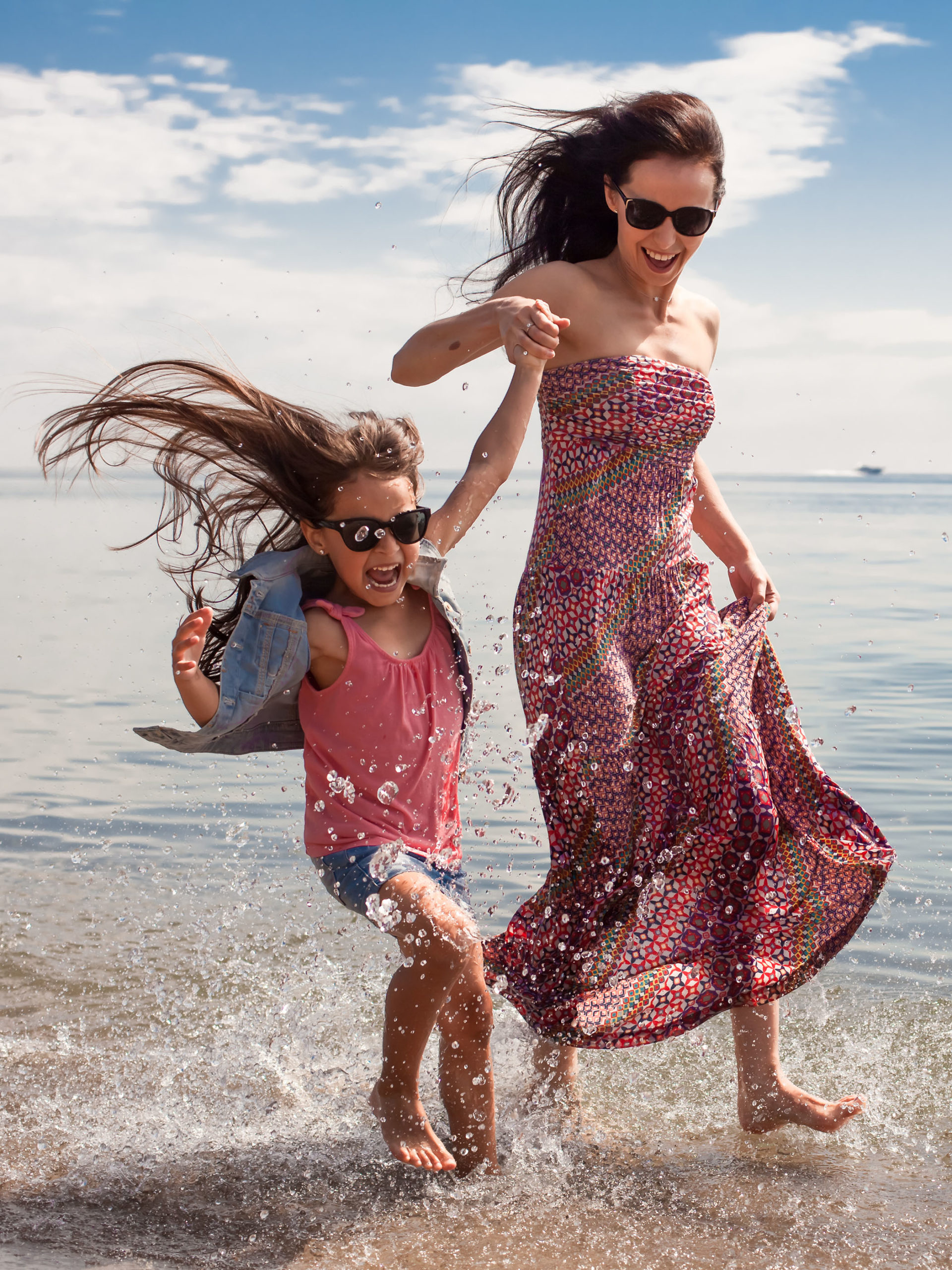 mother and daughter splashing around in water walking along the shore
