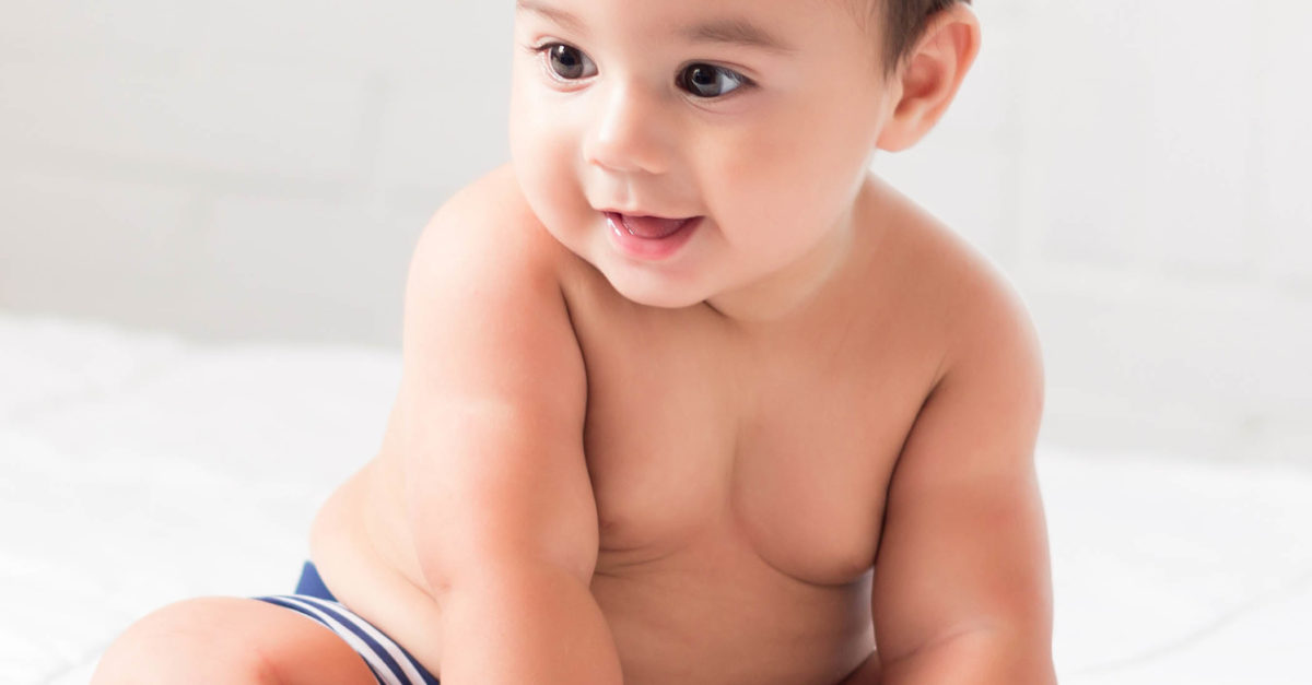 chubby happy baby sitting on bed without a shirt