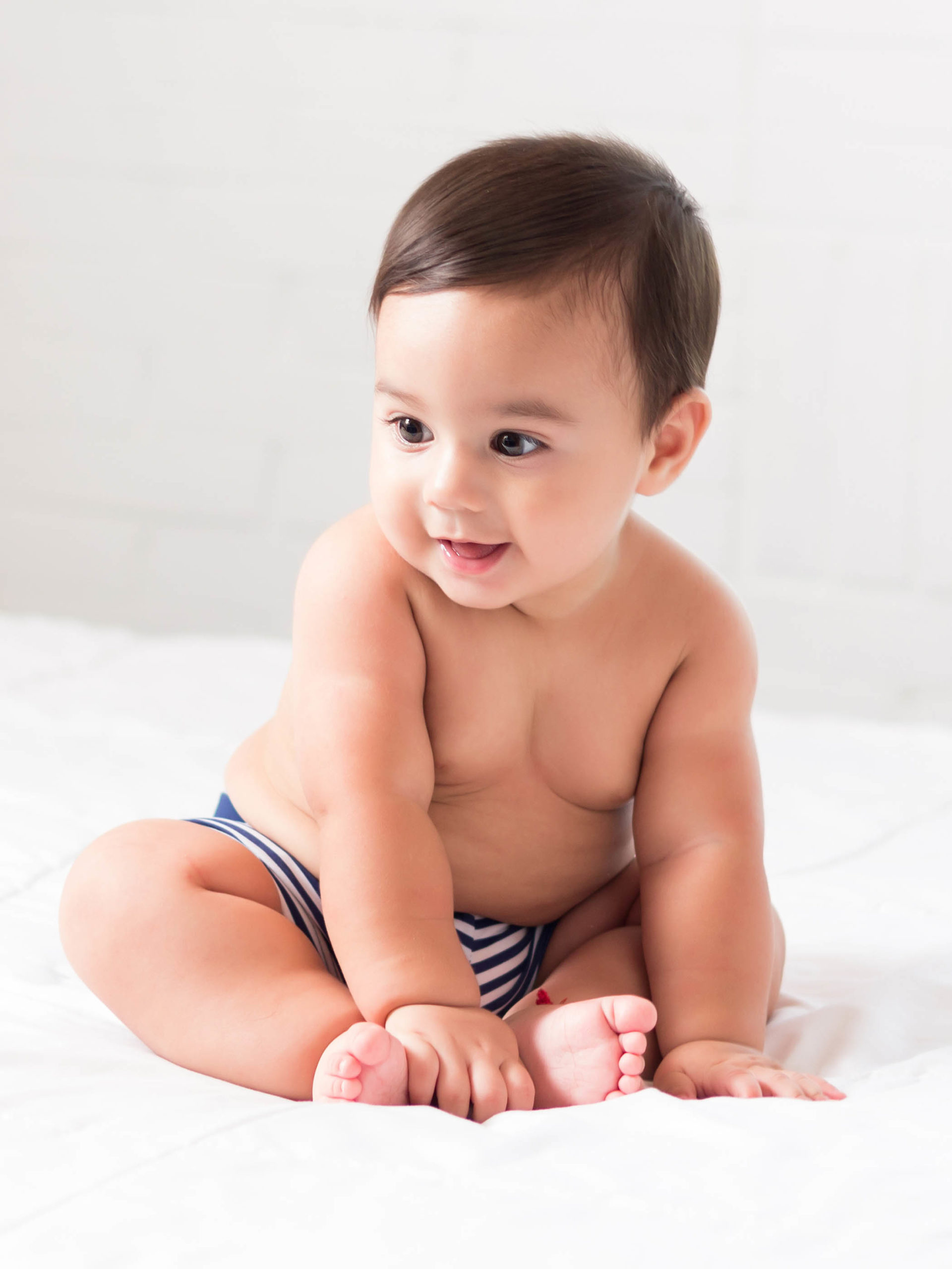 chubby happy baby sitting on bed without a shirt