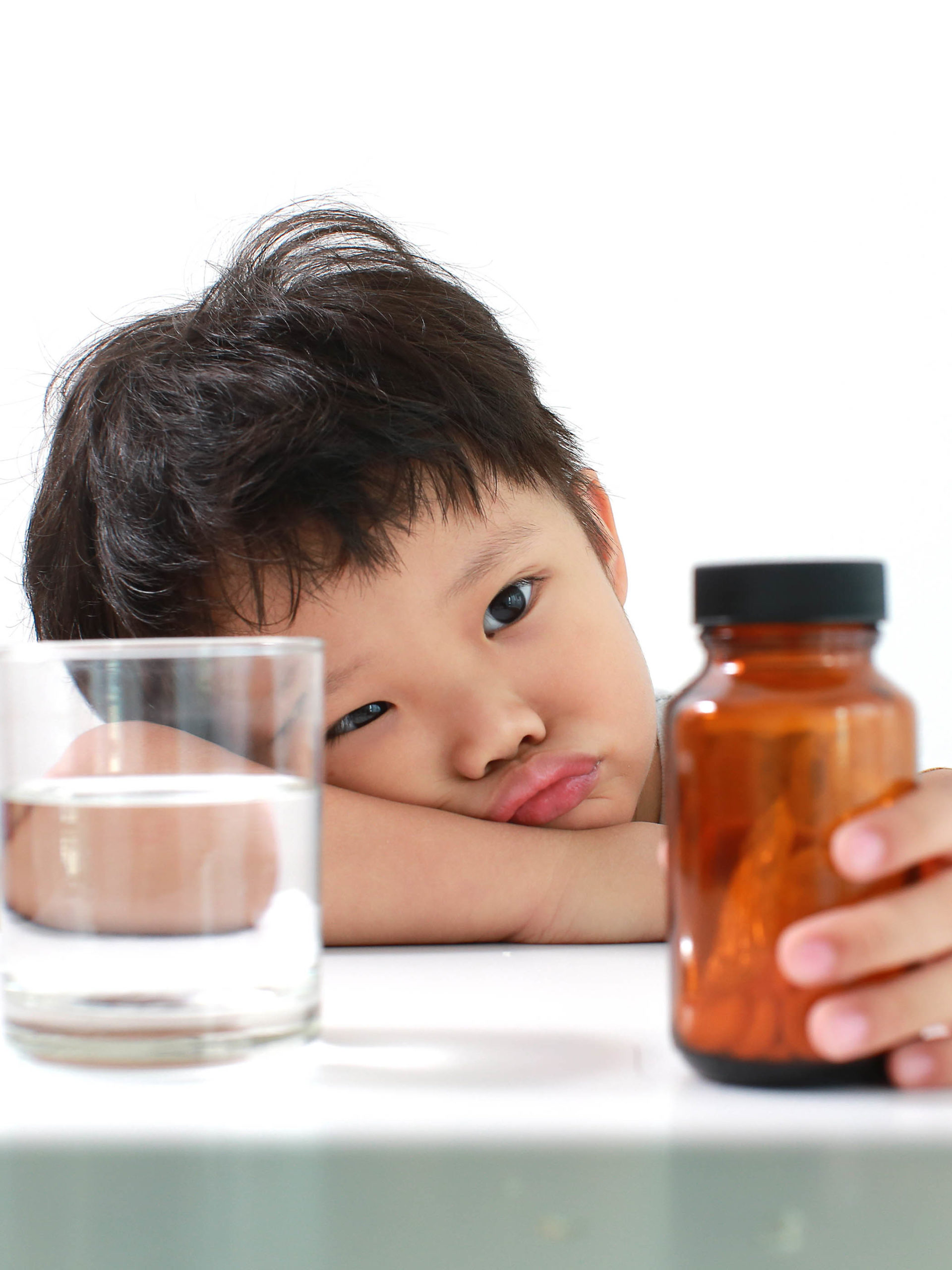 little boy with glass of water refusing to take vitamins