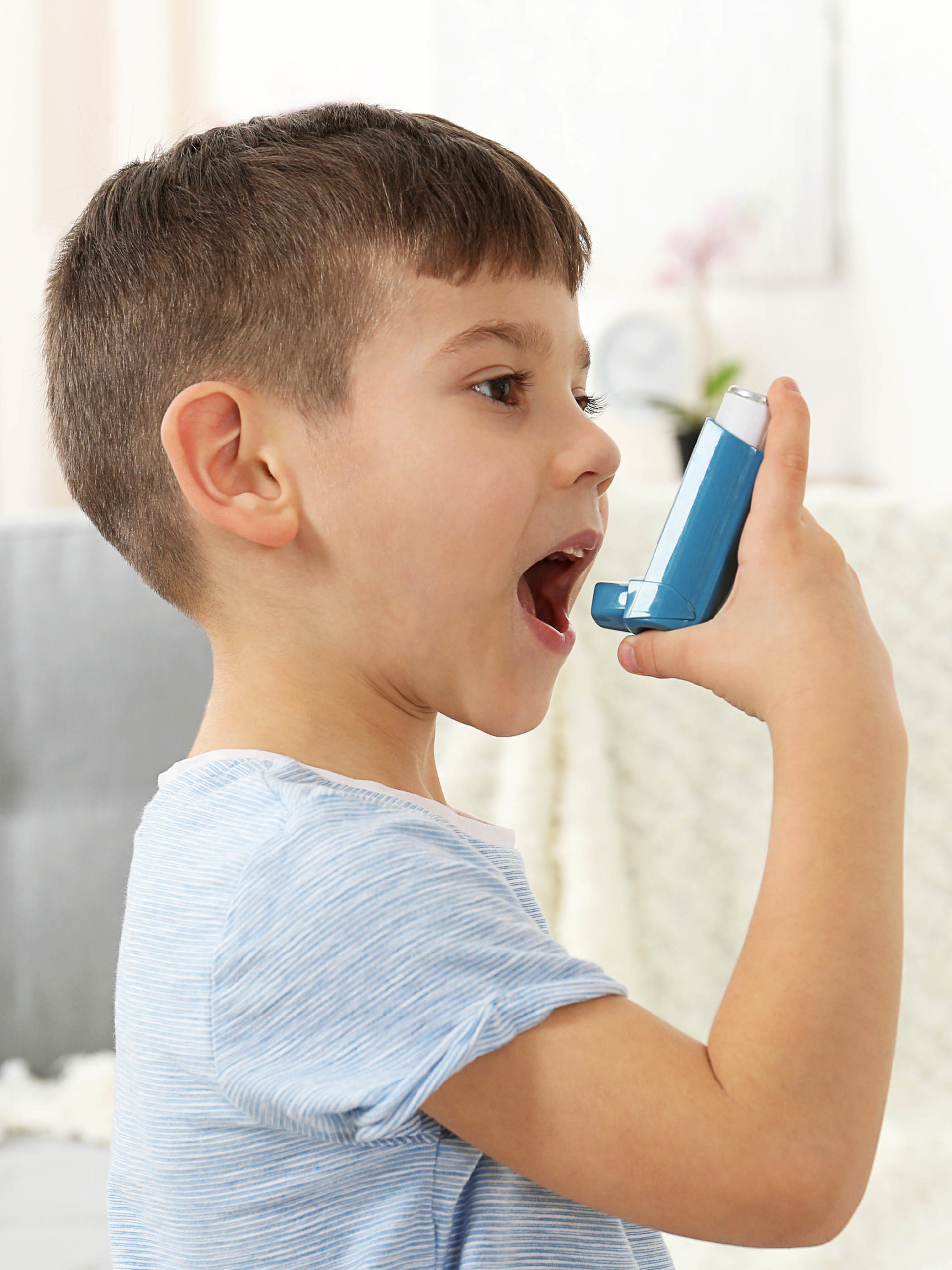 Little boy using blue asthma inhaler at home