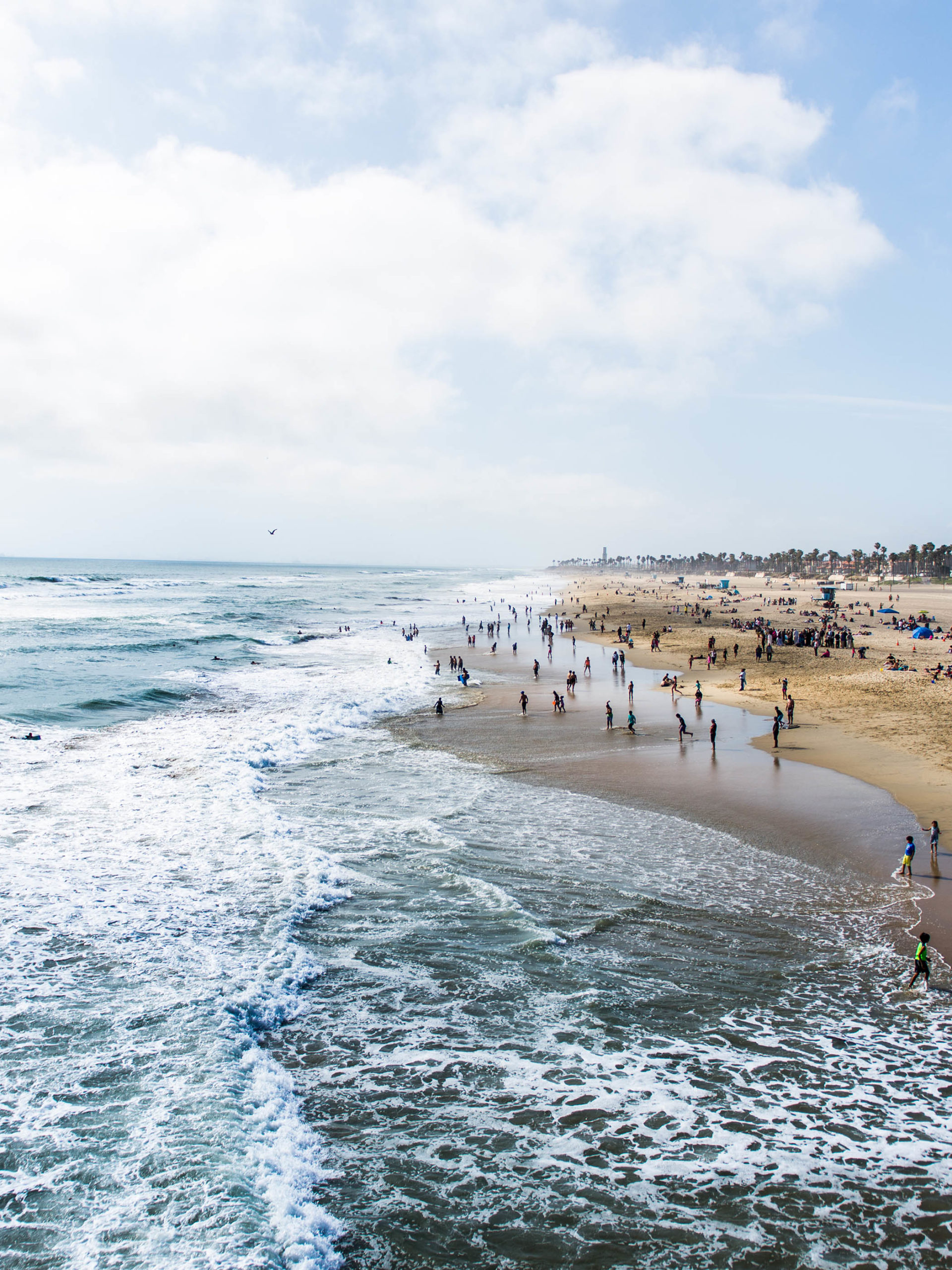 Crowds of tourists and sun bathers having fun and swimming at Huntington Beach