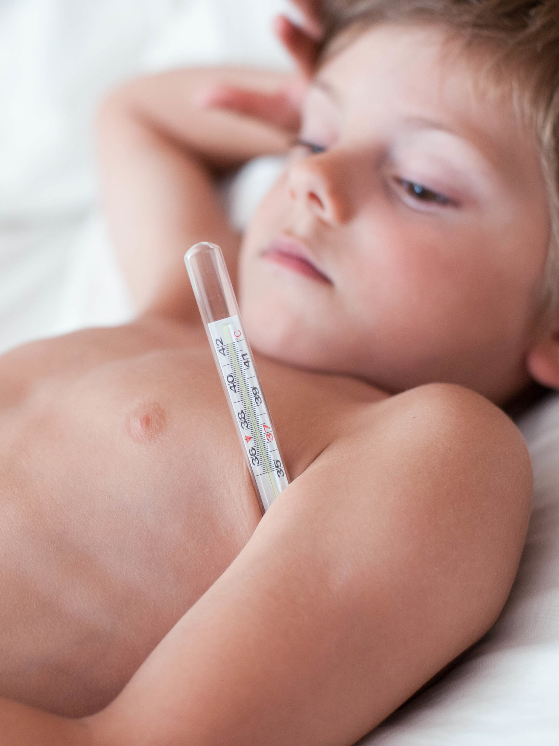 sick little boy with fever lying with thermometer in armpit