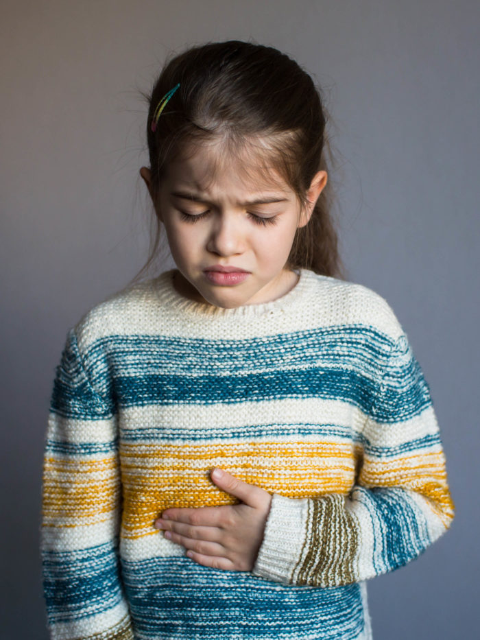 little girl holding her stomach wincing with pain