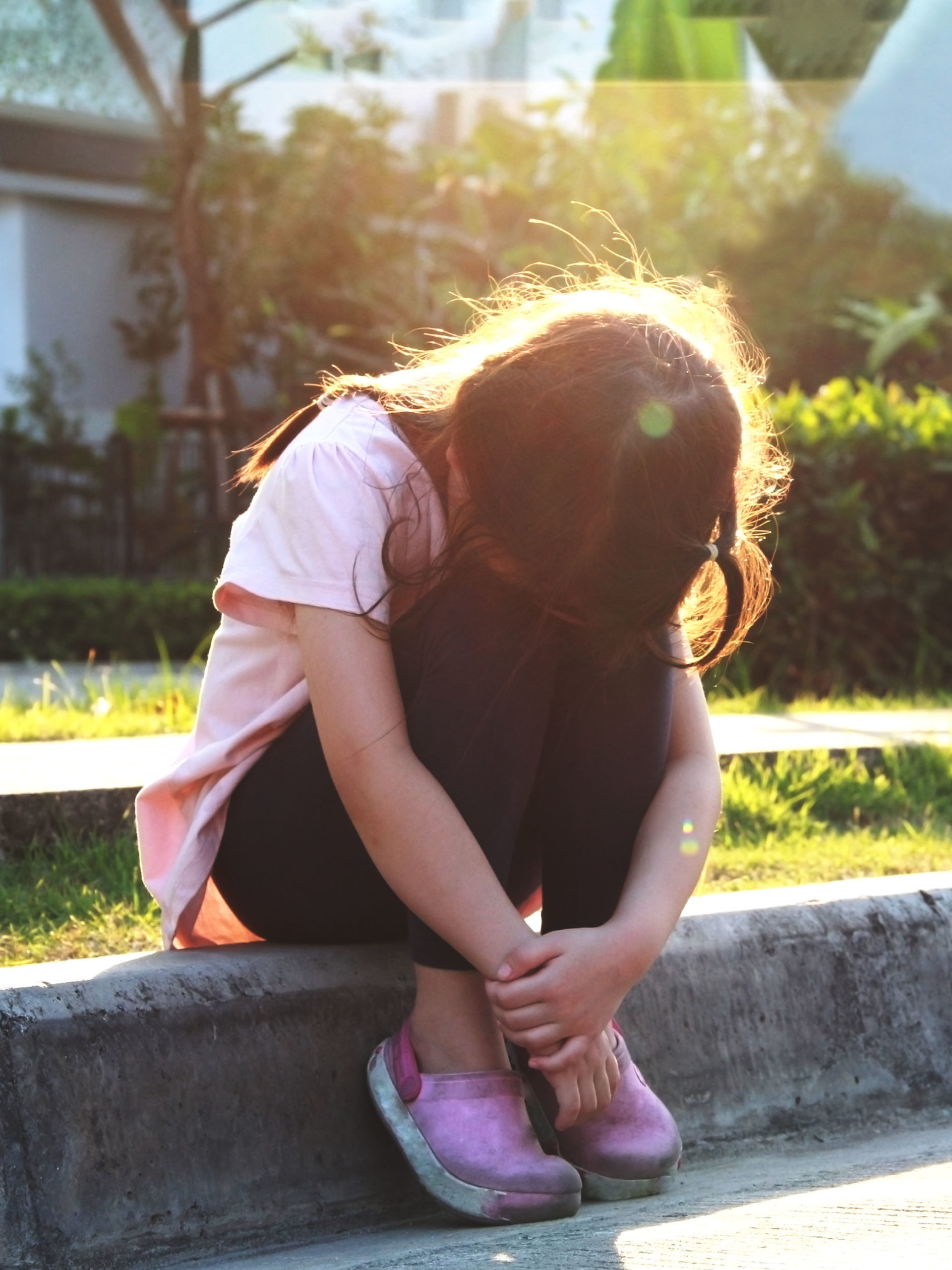 upset girl sitting on the curb hiding her face in her knees