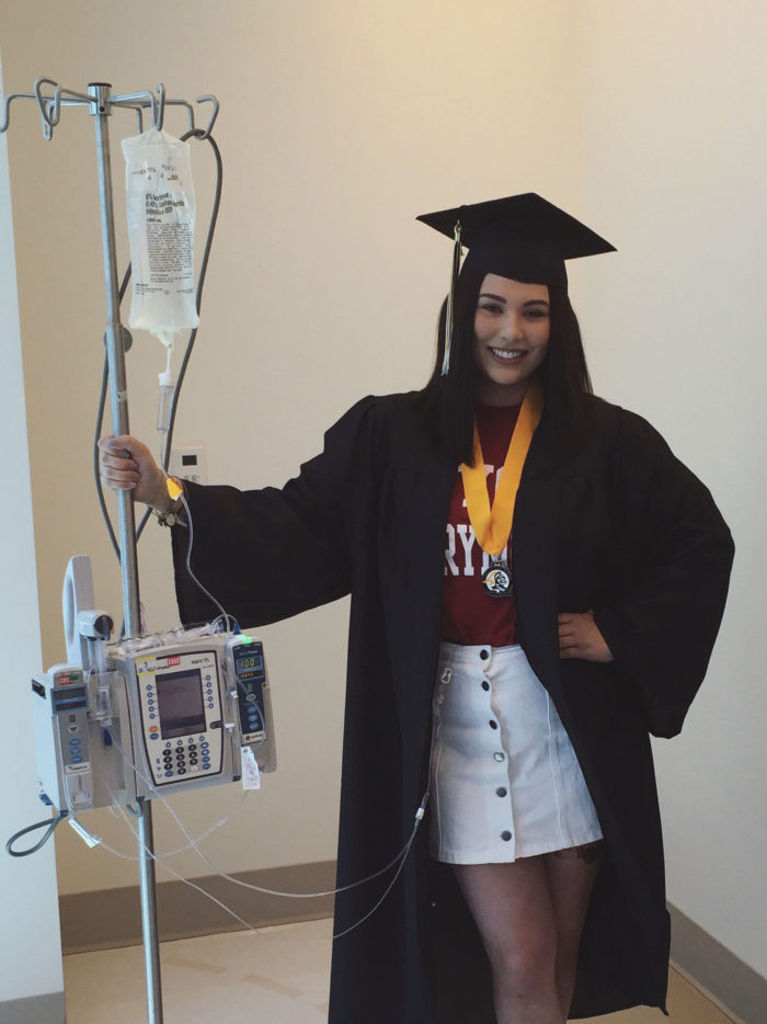 CHOC patient Claire holding on to IV pole while wearing graduation cap and gown