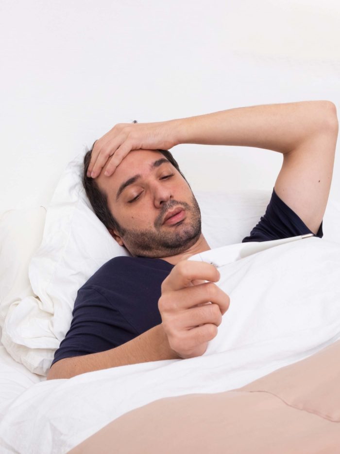 Man checks temperature while sick and laying in bed