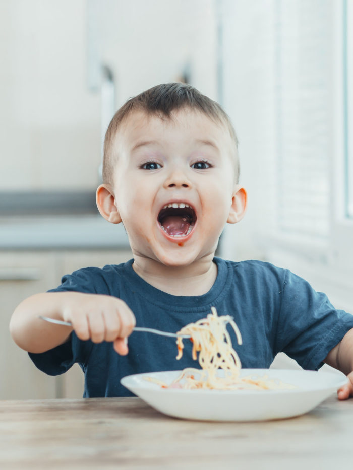 child smiling in the kitchen eating spaghetti