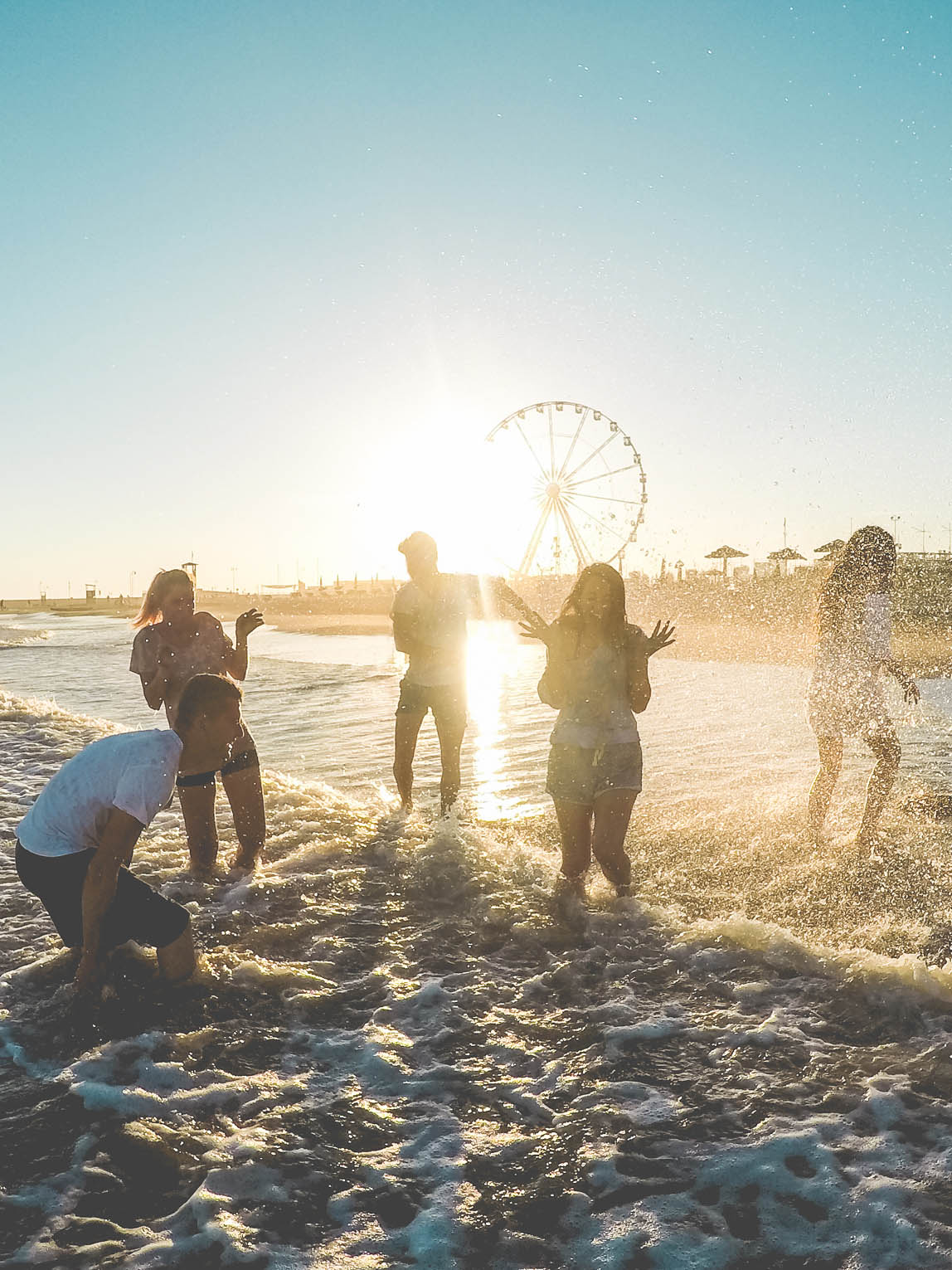 Teenagers splashing in the ocean while walking along the beach having fun