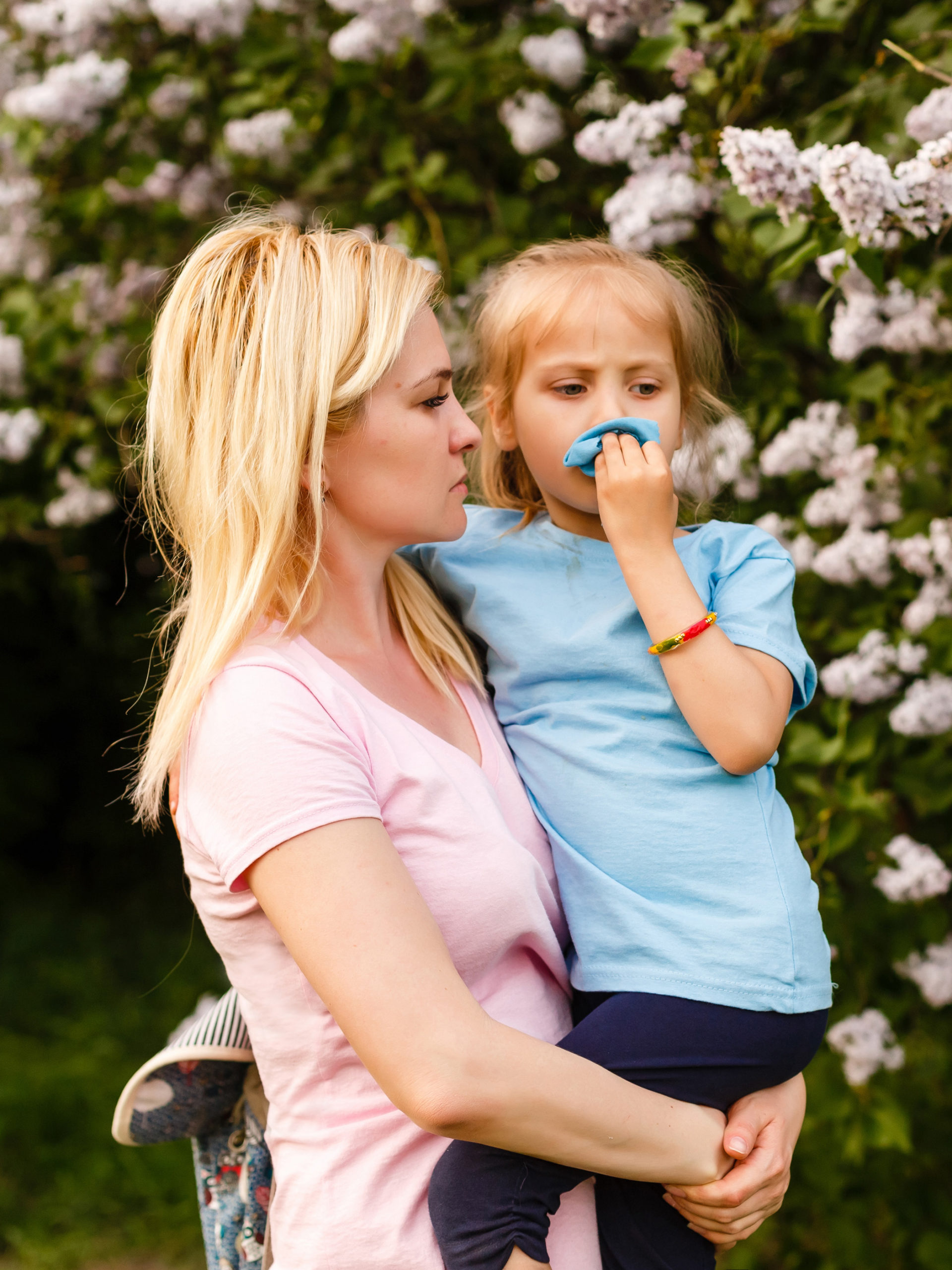 mom holding little girl with allergies blowing her nose surrounded by flowers