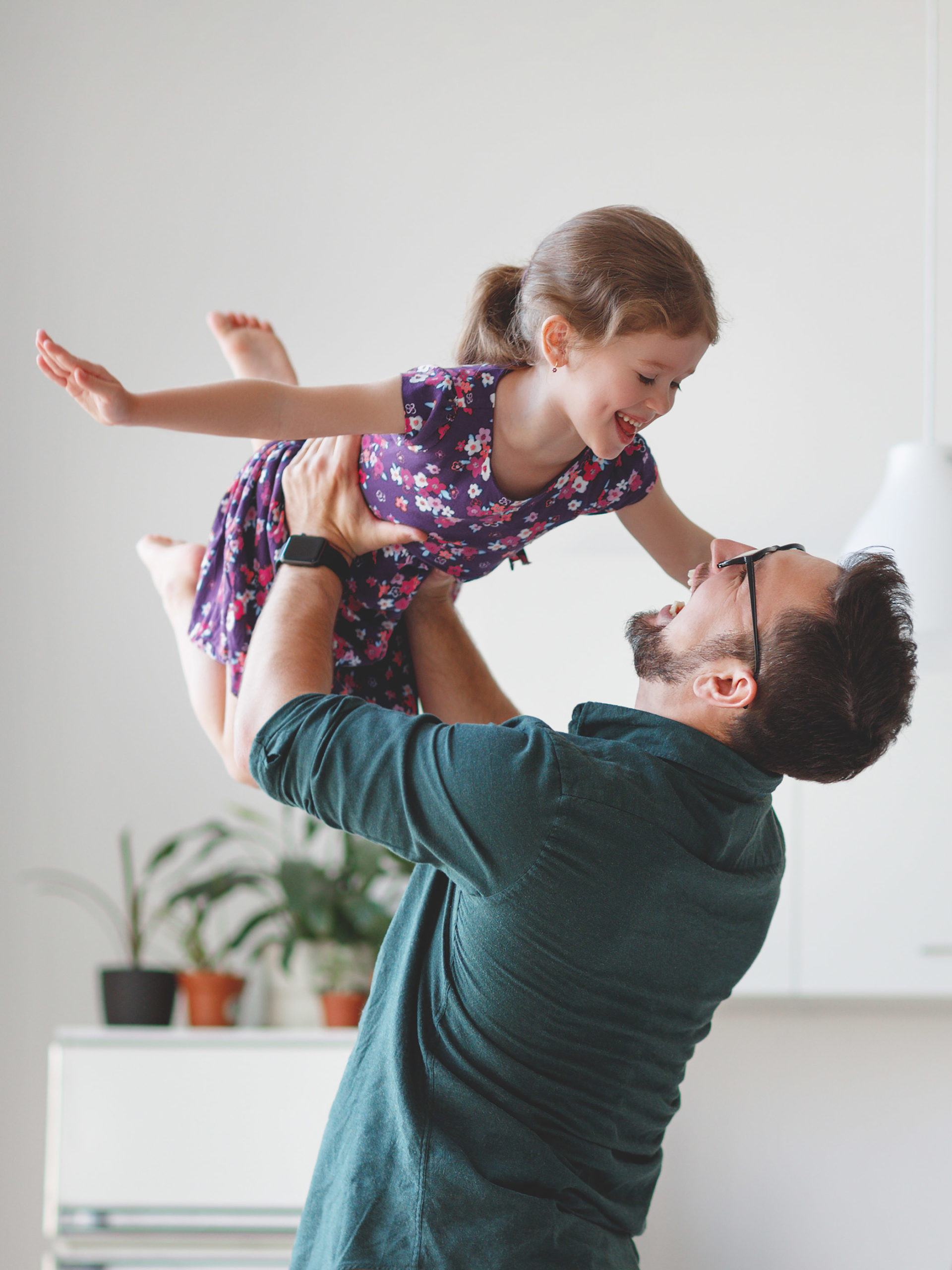 dad playing with daughter holding her above his head while she flies like an airplane