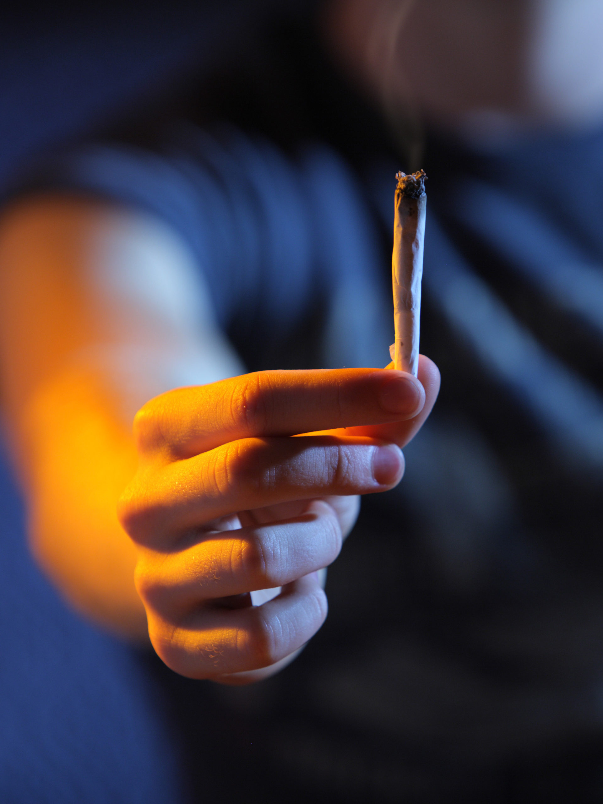 close up of hand holding lit joint with smoke