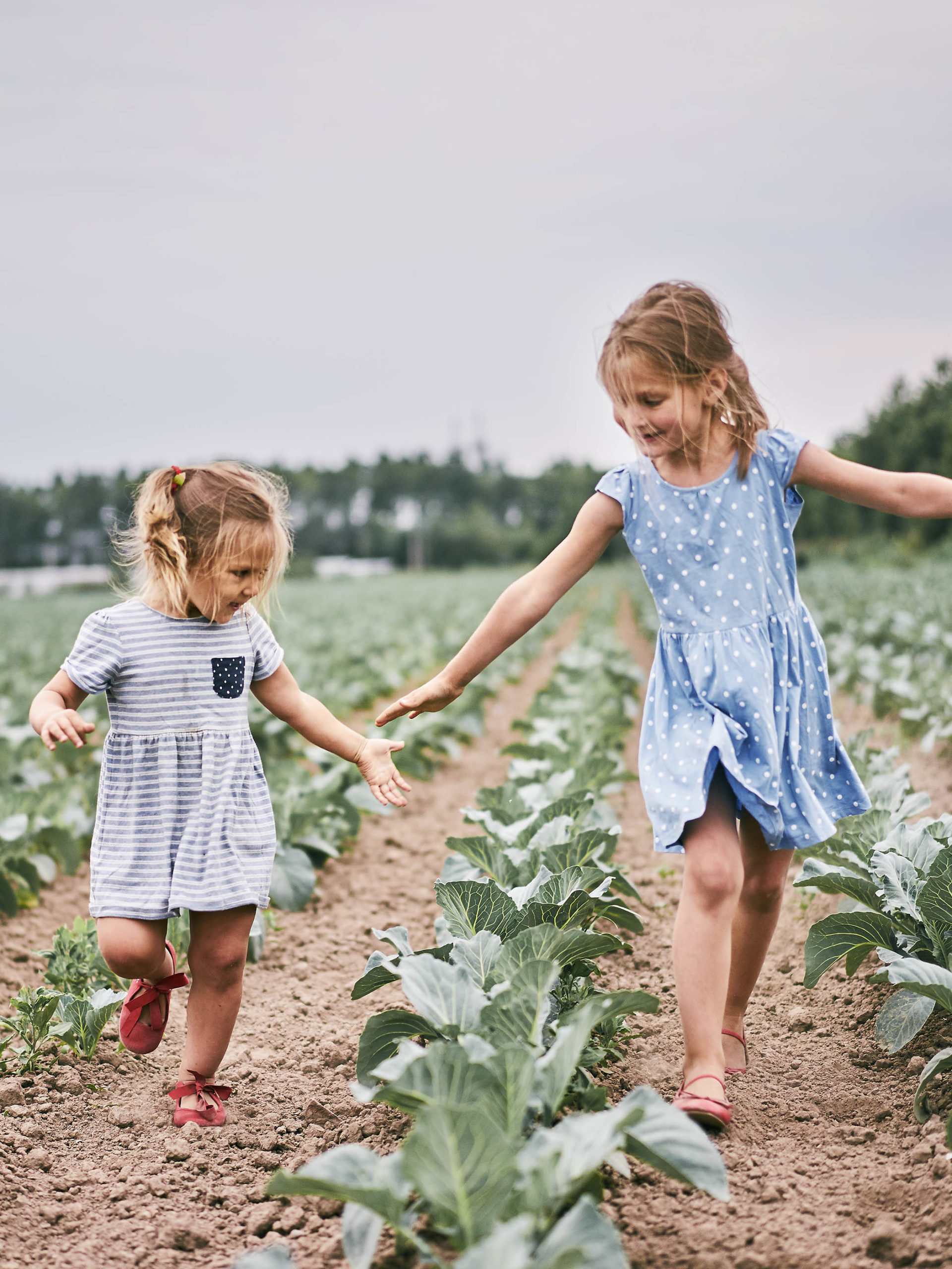 little girls skipping through farm fields on cloudy day