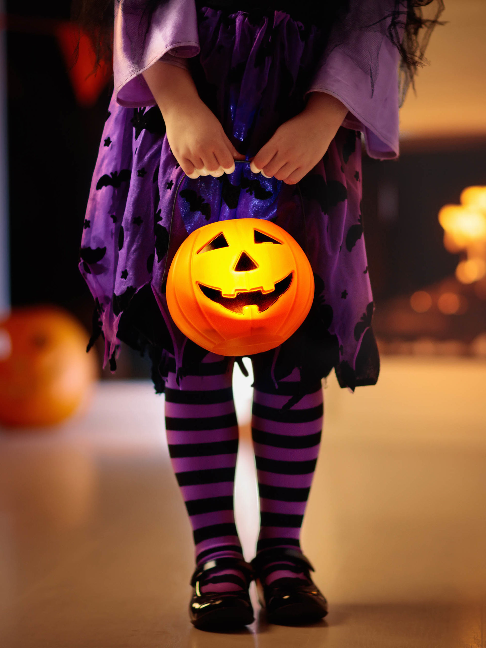 girl in witch costume on Halloween holding candy bucket