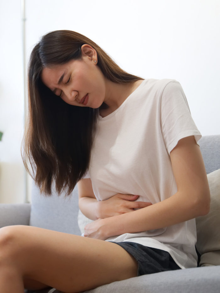 Teen girl having period sitting on sofa in pain