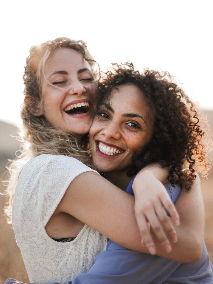 Two female friends hugging and having fun in summer sun