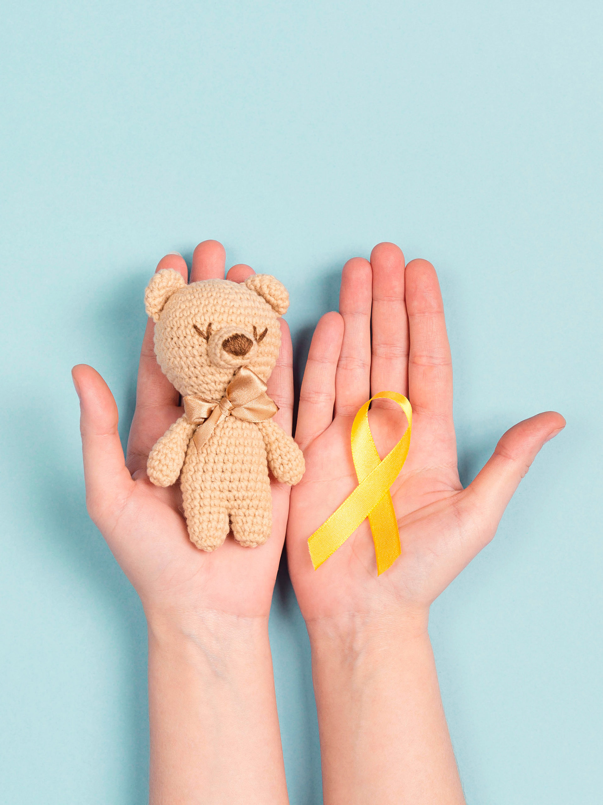 girl's hands outstretched holding a yellow ribbon and small teddy bear