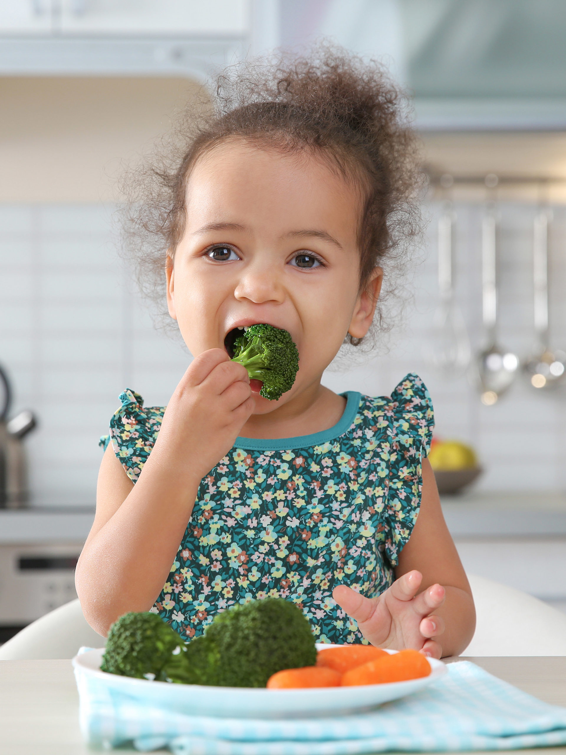 little girl eating broccoli and carrots in kitchen