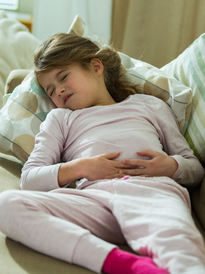 Child lying on sofa in the living room with stomach pain. Hands on belly