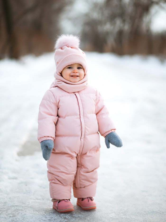 Little beautiful girl in pink jumpsuit smiles in a snowy winter park
