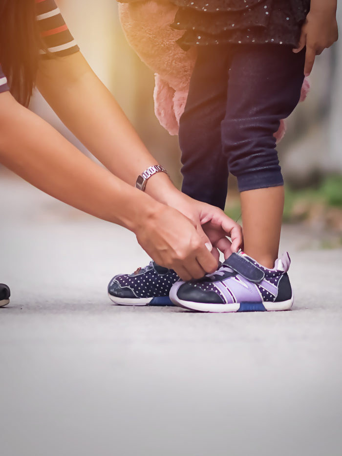 mom in casual suit adjusting the velcro on her little girl's shoes