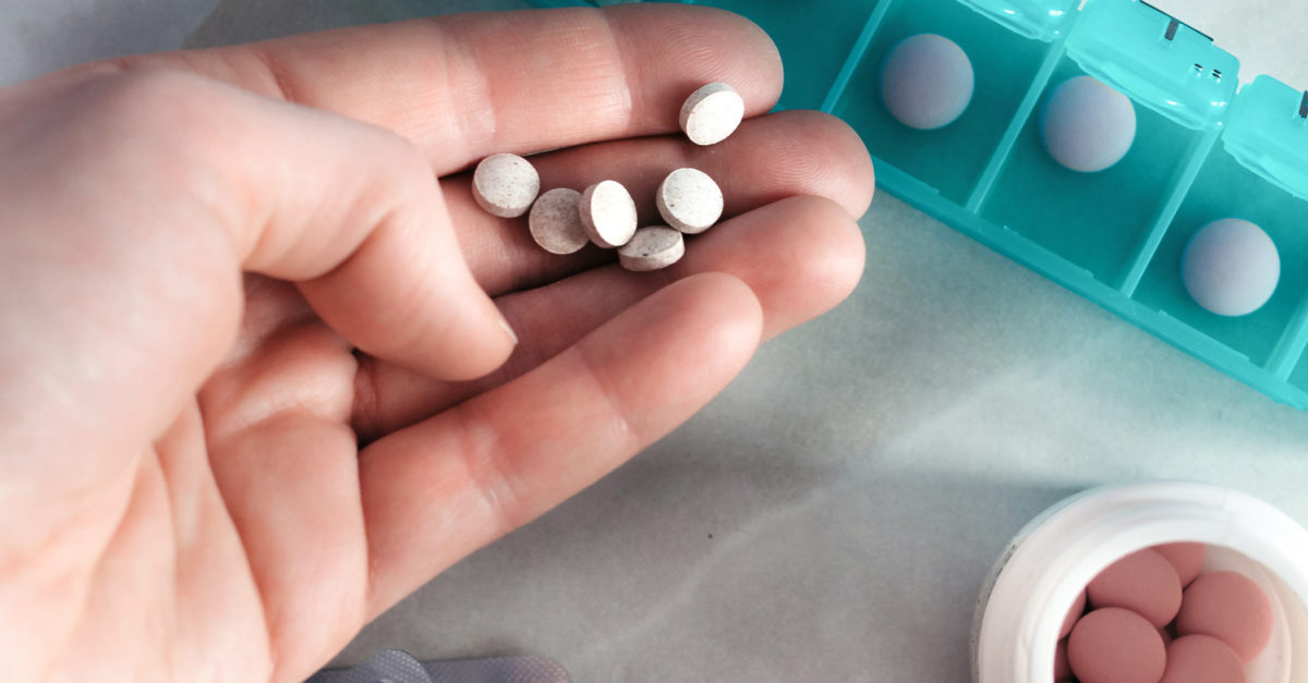 person's hand filling seven-day pillbox with pills