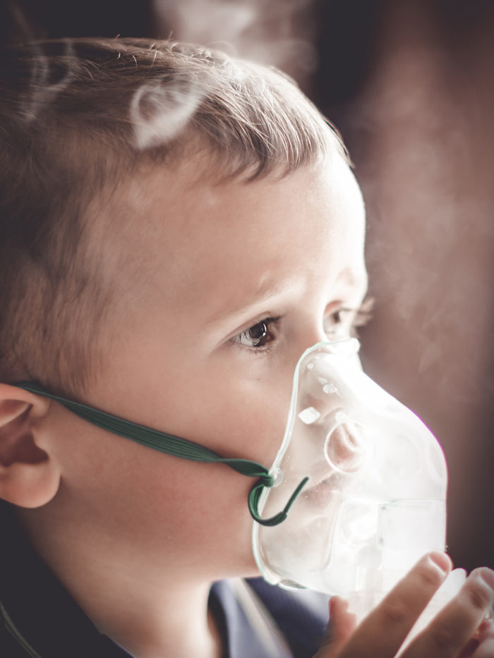 Two year old boy using nebulizer at home for asthma