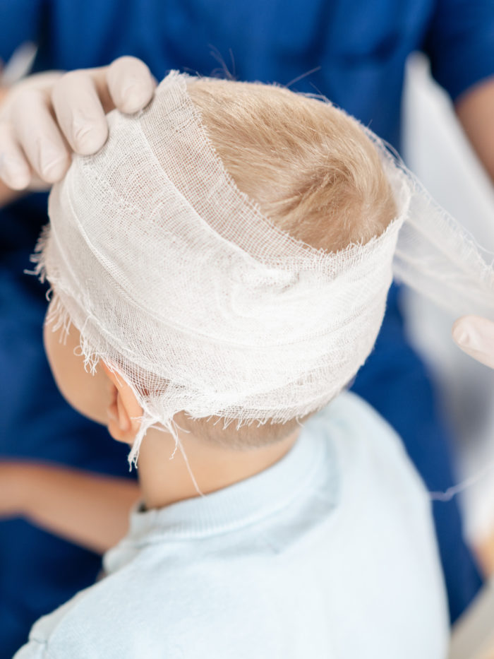 nurse wrapping bandage around the head of young boy