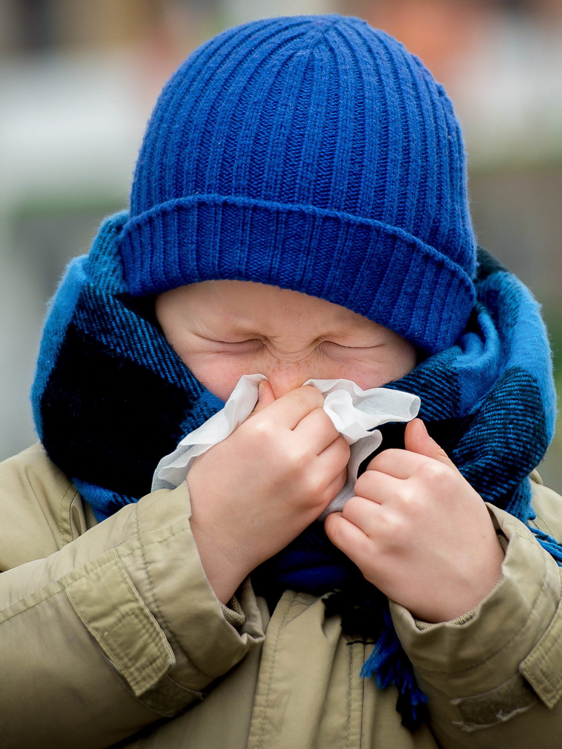 boy wearing beanie, coat and scarf blowing his nose
