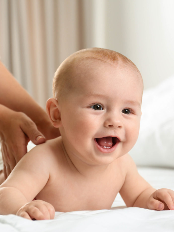 Young woman massaging cute little baby on bed