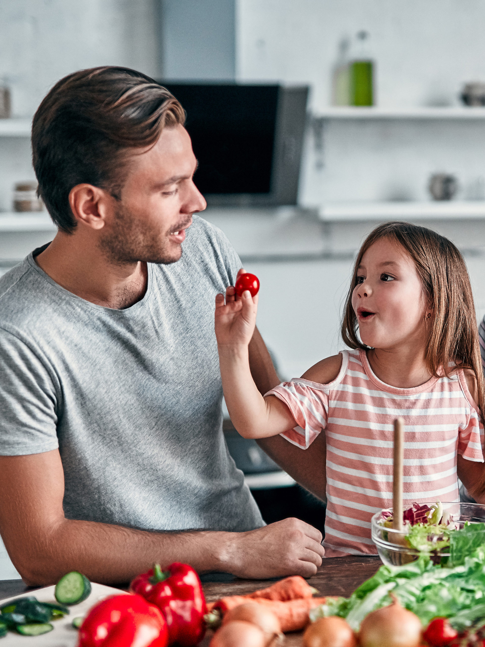 dad and daughter making salad together, little girl feeding dad a cherry tomato