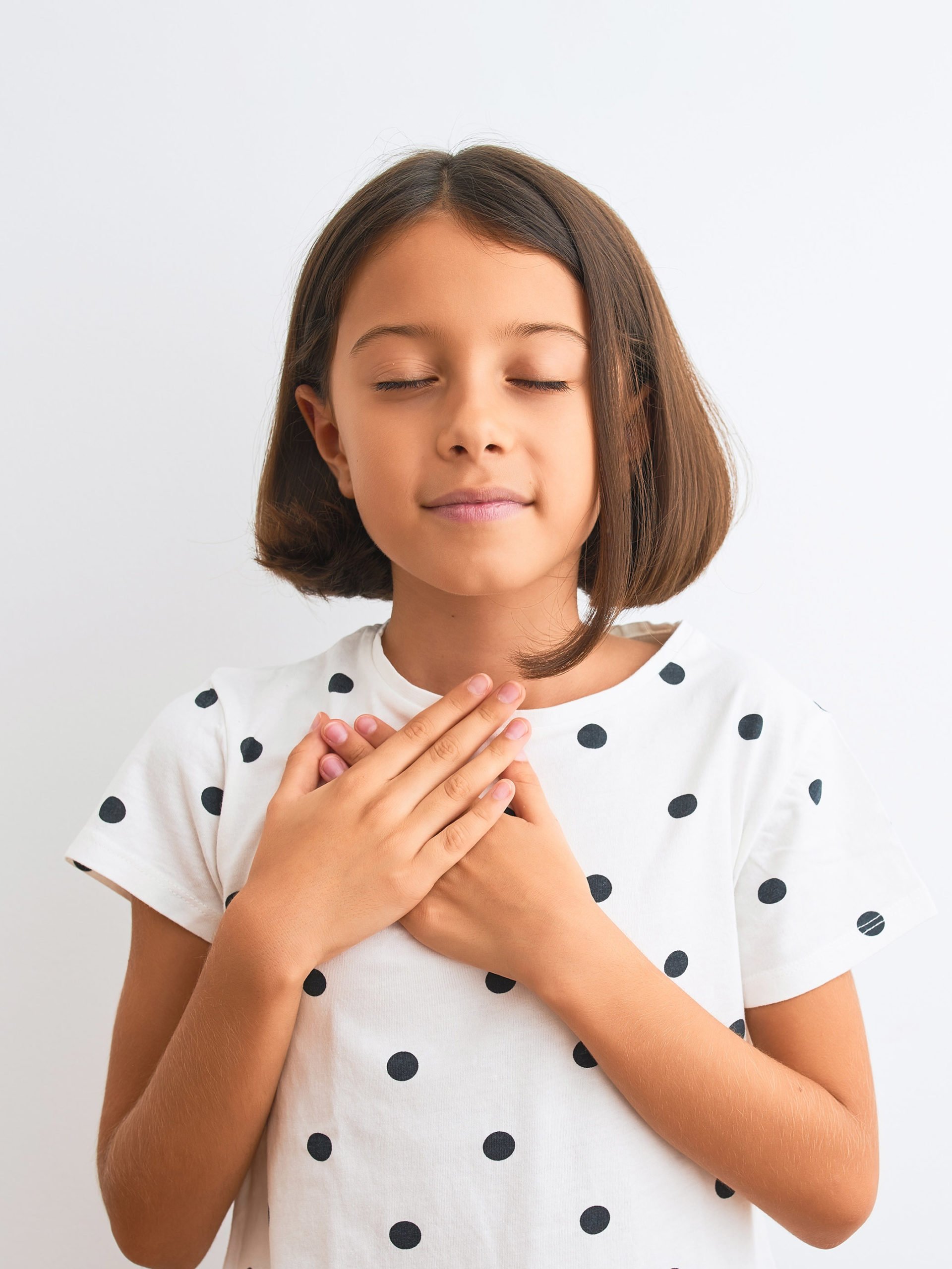 girl wearing polka dot t-shirt standing with hands on chest with closed eyes and grateful expression