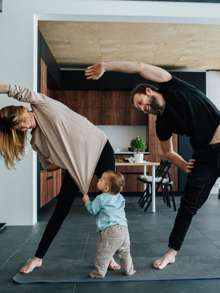 Mother and father doing yoga while their child is pulling mother's shirt
