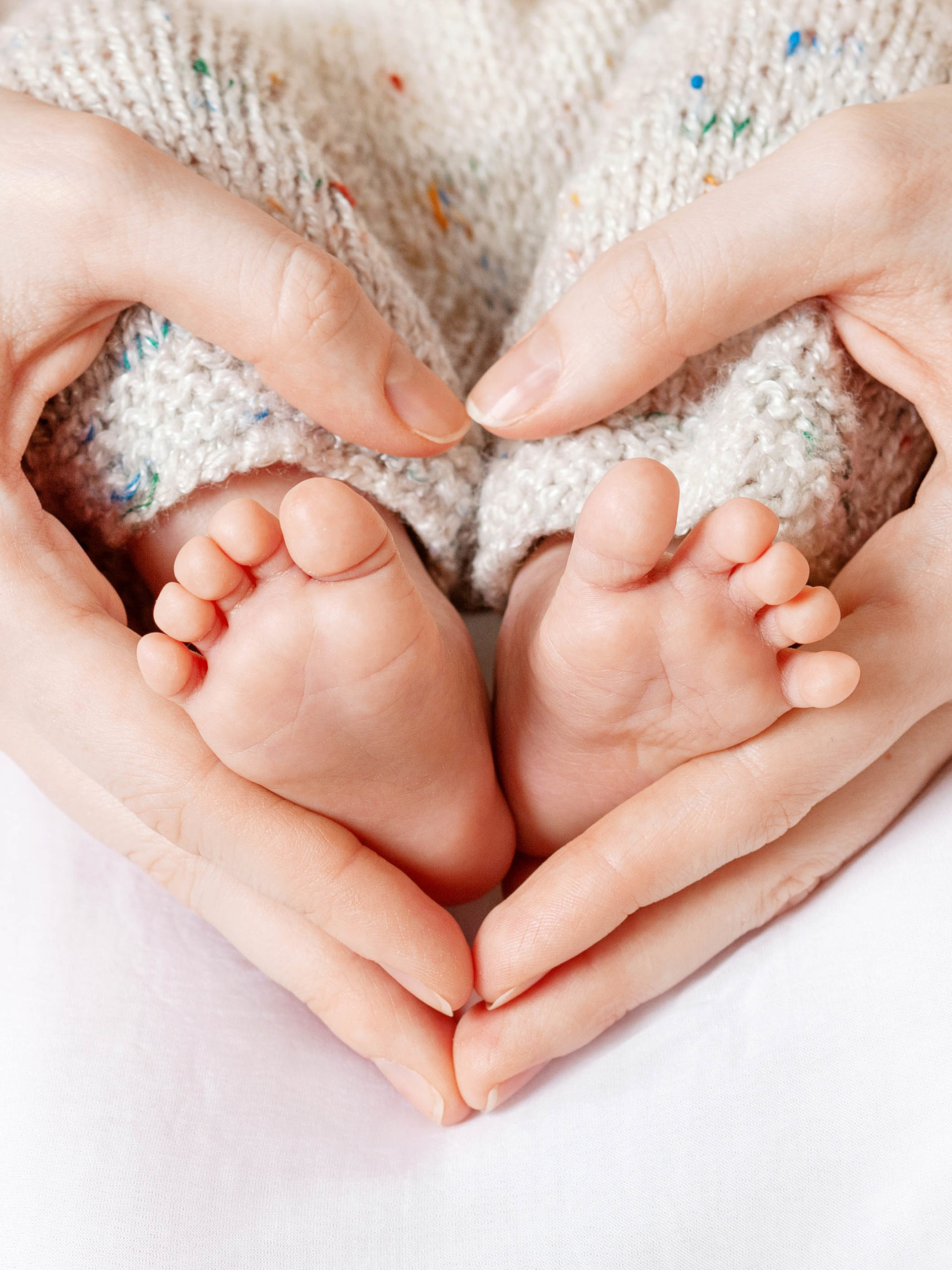 mom holding baby feet in her hands making a heart shape
